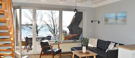A modern living room with a sofa, chairs, a coffee table, and a view of a building through large windows.