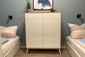 Une chambre à coucher avec un lit, une armoire et une étagère fixée au mur, sur laquelle se trouvent une plante et une horloge.