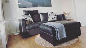 Ein modernes Wohnzimmer mit einem schwarzen Ledersofa, einem passenden Hocker und einem großen abstrakten Gemälde darüber.
