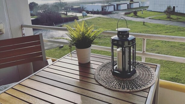 Ein Balkon mit Holztisch, einem Blumentopf und einer Laterne.