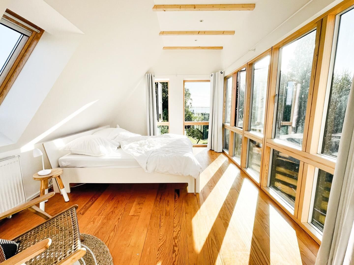Een slaapkamer met een schuine kap, grote ramen, een bed, een klein tafeltje en een stoel.