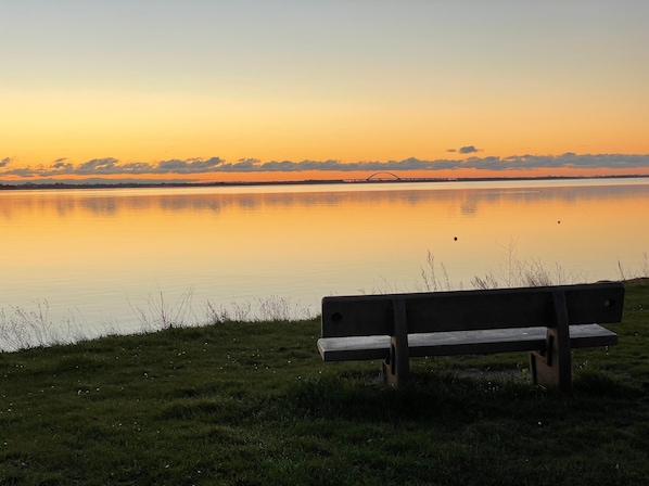 En bänk vid en stilla sjö i solnedgången, med en bro i fjärran.