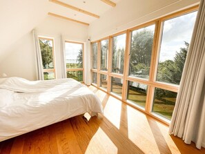 A bedroom with a large bed, multiple windows, and a view of greenery. - Seehaus in Orth on Fehmarn right by the sea - filming location "Schwanitz" (Fehmarn)