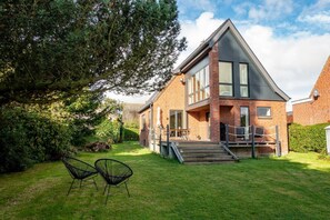 A two-story brick house with a large front yard, a staircase leading to the entrance, and two chairs in the yard. - Seehaus in Orth on Fehmarn by the sea—filming location for "Schwanitz" (Fehmarn)