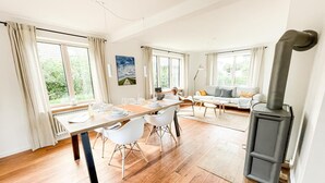 Ein modernes Wohnzimmer mit Essbereich, großen Fenstern und einem Kaminofen.