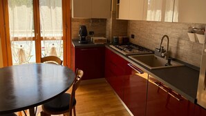 Een kleine keuken met een gasfornuis, een wastafel en een koffiezetapparaat. Er is een eettafel met stoelen en een uitzicht door een glazen deur.