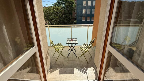 Een balkon met twee gele stoelen en een klein tafeltje, met uitzicht op een gebouw en bomen.