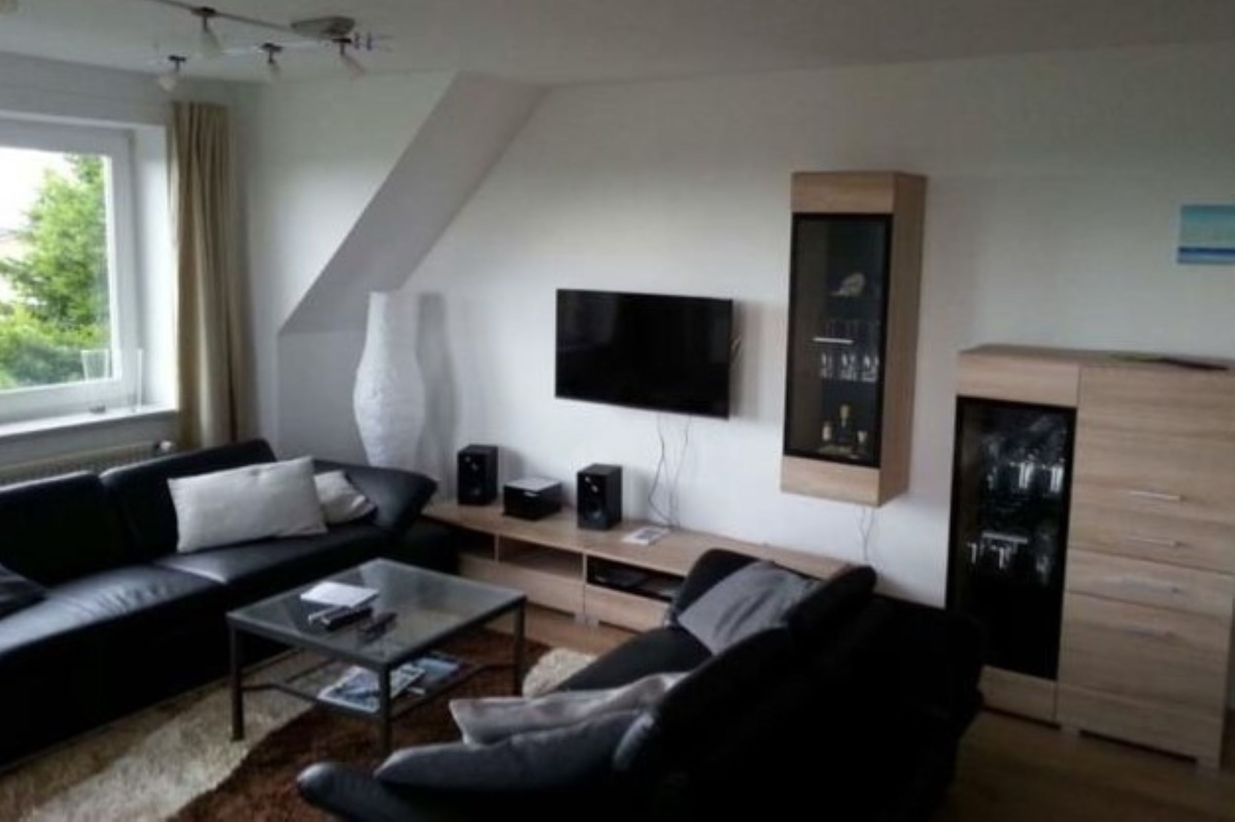 A modern living room with a black sofa, a coffee table, a flat-screen TV mounted on the wall, and a wooden cabinet.