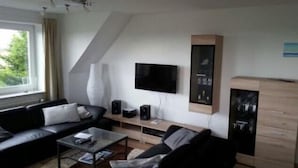 A modern living room with a black sofa, a coffee table, a TV, and a cabinet. - Vacation apartment with sea view on Fehmarn - Seeblick Marienleuchte (Fehmarn)