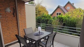 Un balcon avec une table et des chaises, une vue sur un immeuble en briques et un ciel dégagé.