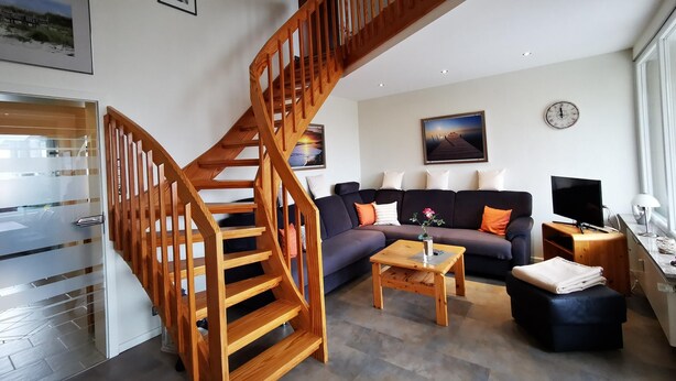 Un salon moderne avec un escalier en bois, un ensemble de canapés, une table basse et un téléviseur.