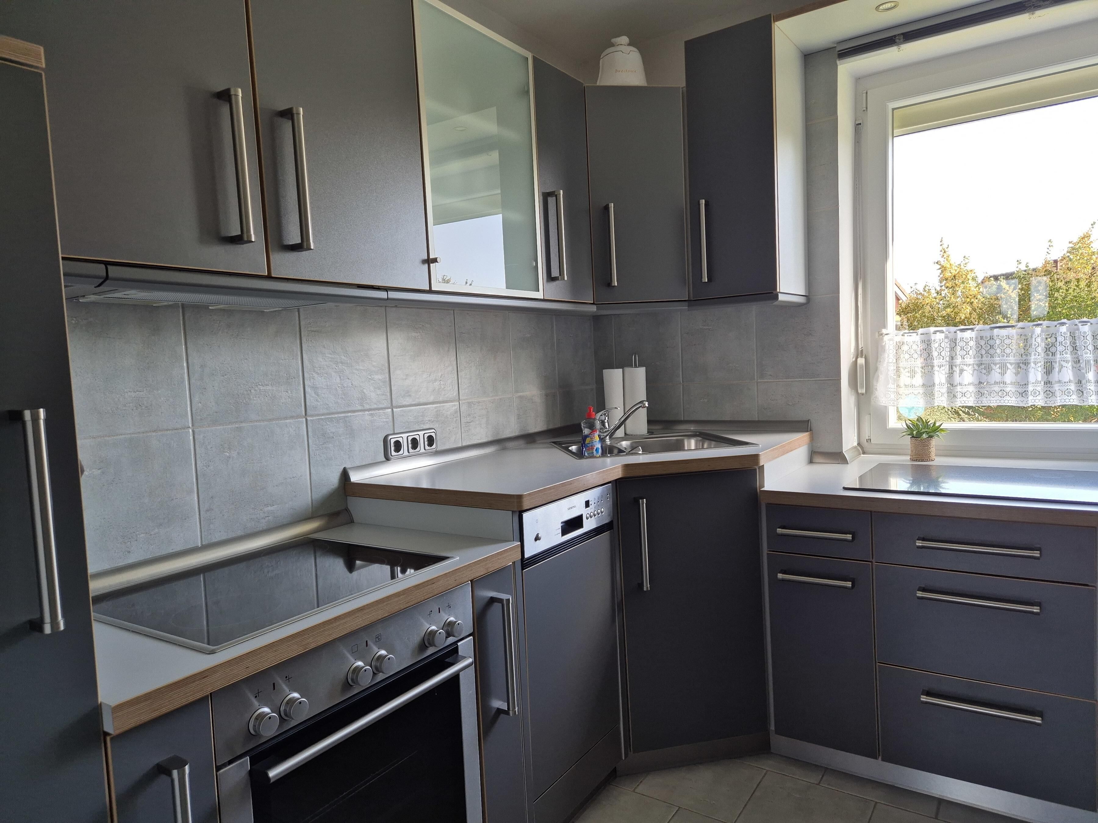 A modern kitchen with grey cabinets, a stainless steel oven, and a window with a view of the outside.