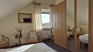 Une chambre à coucher avec un grand lit, une armoire, un miroir et deux fauteuils en osier.