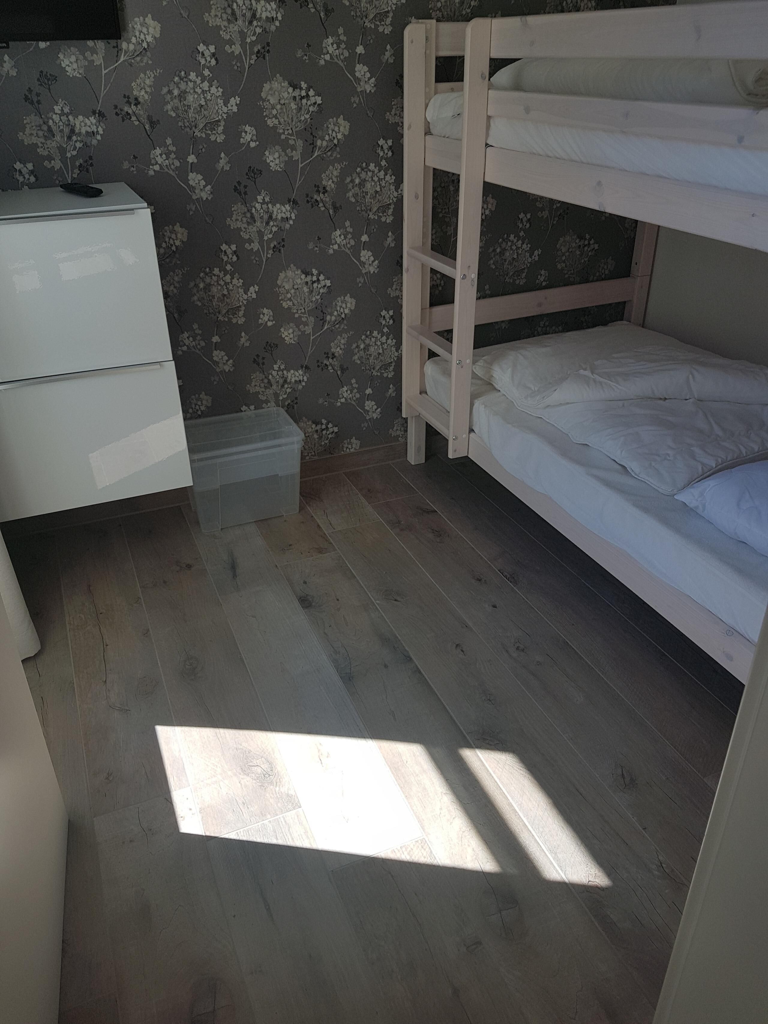 Un dormitorio pequeño y ordenado con una cama individual sobre otra, un aparador y una caja de almacenamiento pequeña.