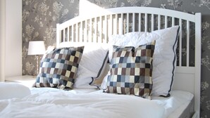 A neatly made bed with white bedding and checkered pillows, a white headboard, and floral wallpaper. - Beach residence Vogelflug App. 10 - spacious & close to the beach (Fehmarn)
