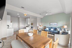 A spacious living area with a dining table, sofas, and a kitchen in the background. - Hope’s Sunrise 2BR Condo with Free Beach Service (Destin)