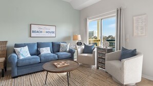 Una sala de estar con un sofá azul, un sillón beige, una mesita de centro y un amplio ventanal con vistas a edificios.