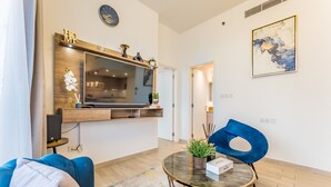 Un salon moderne doté d’un grand téléviseur à écran plat, d’un canapé bleu, d’une table basse ronde ornée d’une plante et d’un fauteuil bleu.