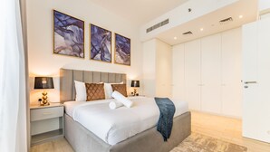 Une chambre à coucher moderne avec un grand lit, des tables de chevet avec des lampes, une armoire et des œuvres d’art abstraites accrochées au mur.