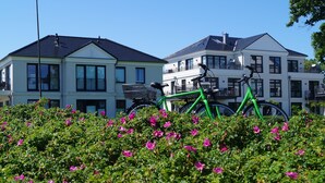 En rad moderna tvåvåningshus med balkonger, omgivna av frodiga, gröna buskar med rosa blommor.