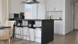 Ett modernt kök med en central köksö, barstolar, en mikrovågsugn och en kaffemaskin.