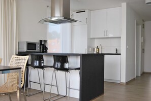 A modern kitchen with a central island, bar stools, a microwave, and a coffee machine. - Luxurious vacation apartment with breathtaking sea views on the Baltic Sea! (Fehmarn)