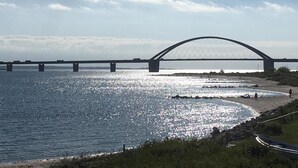 En stor bro som sträcker sig över en vattenyta, med en strand och ett grönområde i förgrunden.