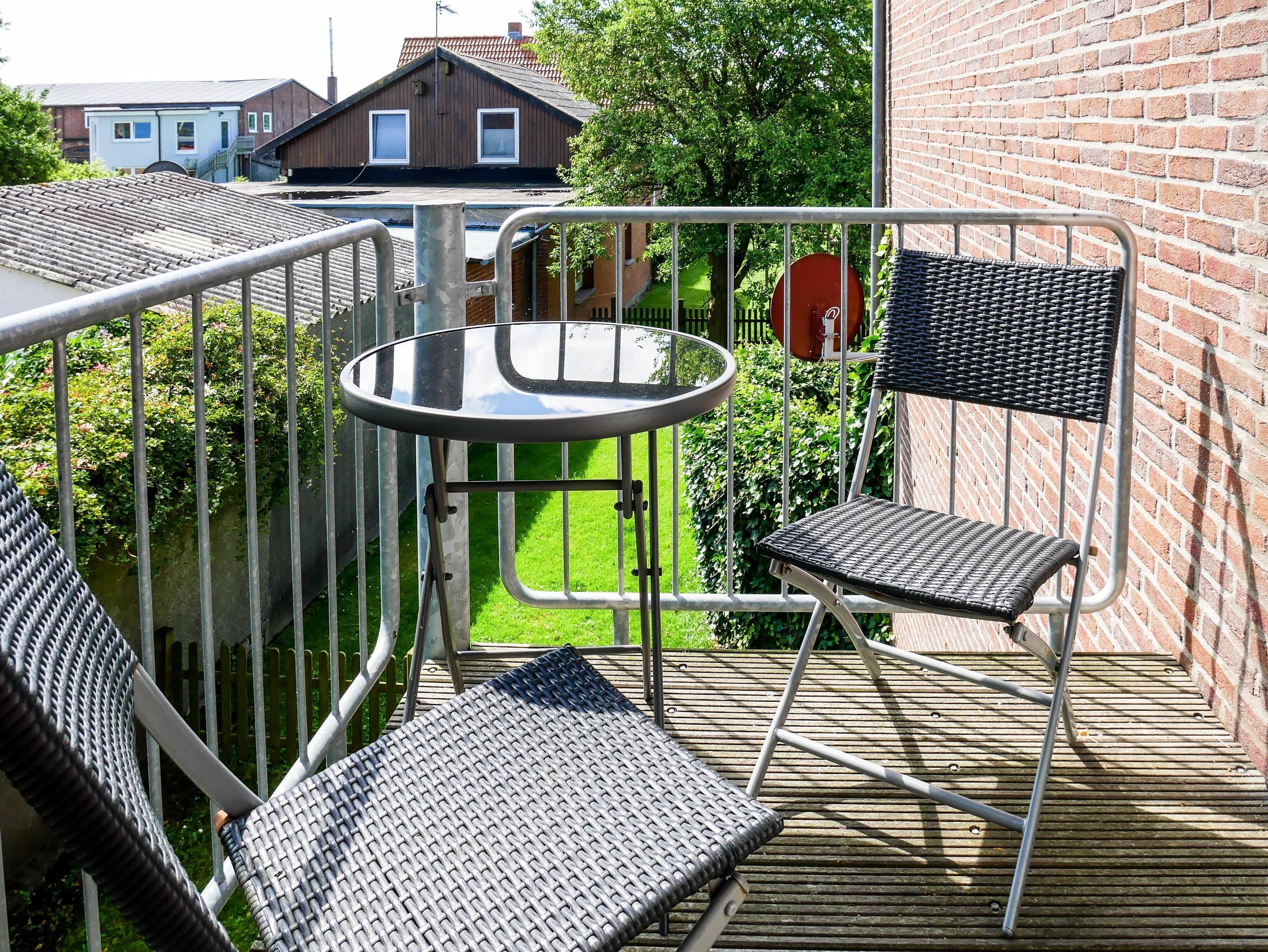 A balcony with a round table and two wicker chairs.