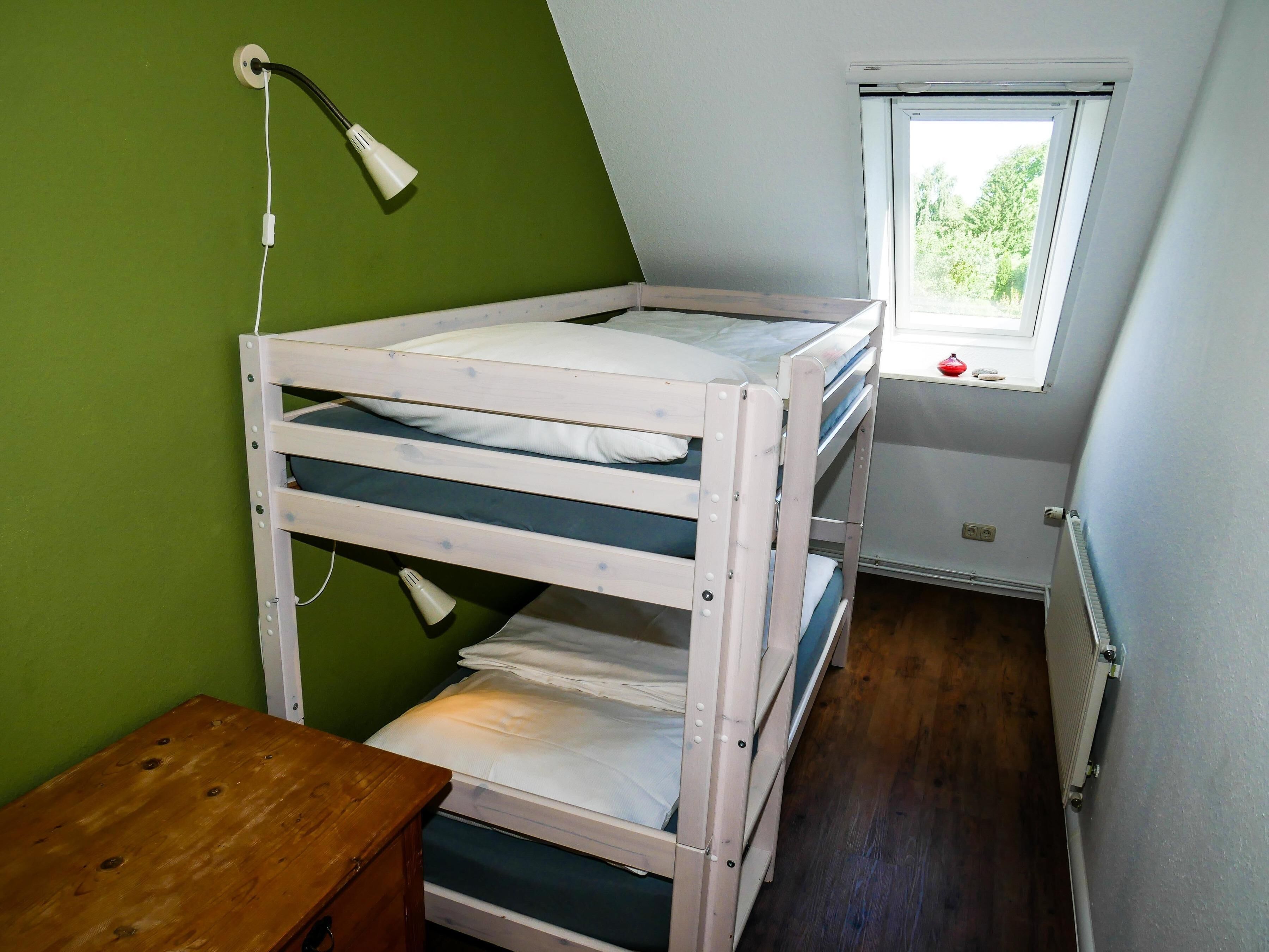 A bunk bed in a room with a sloped ceiling, a window, and a radiator.