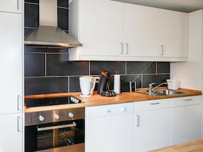 Eine moderne Küche mit weißen Schränken, einer schwarzen Küchenrückwand, einer Edelstahl-Dunstabzugshaube, einer Kaffeemaschine, einem Wasserkocher, einem Toaster und einem Geschirrspüler.