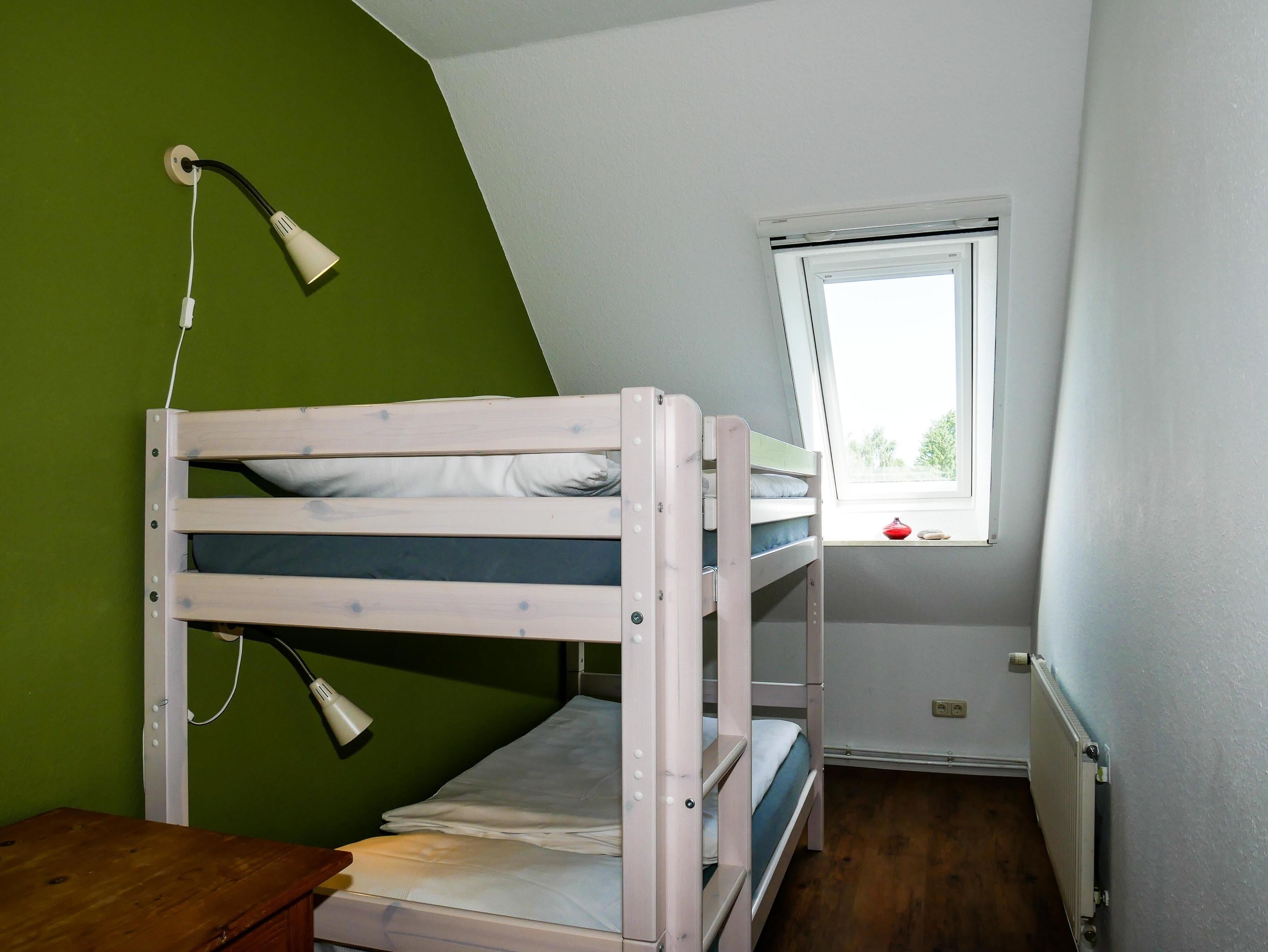 A bunk bed room with a window, a desk, and a lamp.