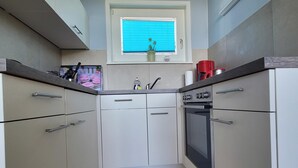 Una cocina compacta con armarios blancos, horno empotrado y ventana con persianas.