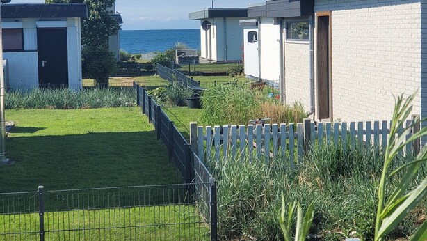 Zona residencial costera con casas modernas, un césped y una valla de madera.
