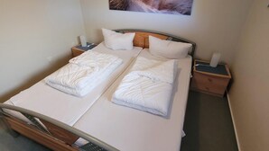 Una cama doble con estructura de madera, dos almohadas, una mesita de noche con lámpara y un cuadro en la pared.