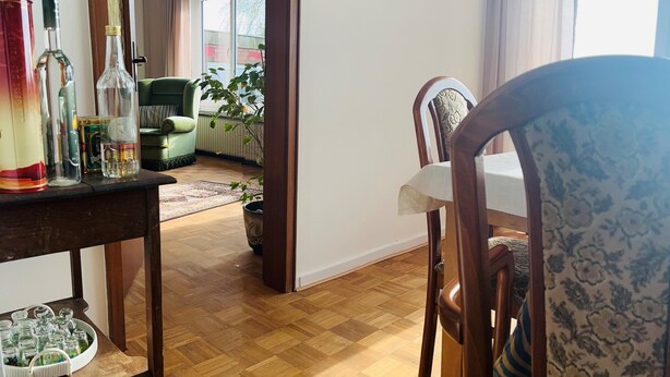 A dining area with wooden flooring, a table with chairs, and a view of a living room with a sofa and a window. - Vacation home Zur Alten Mühle - spacious living in Orth (Schwanitz) with garden & T (Fehmarn)