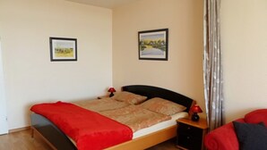 A single bed with a red blanket, a nightstand with a lamp, and a red chair. - Relax in the cozy vacation apartment on the Baltic Sea in Fehmarn! (Fehmarn)