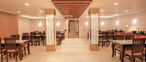 A spacious dining area with multiple tables and chairs, wooden ceiling panels, and decorative light fixtures.