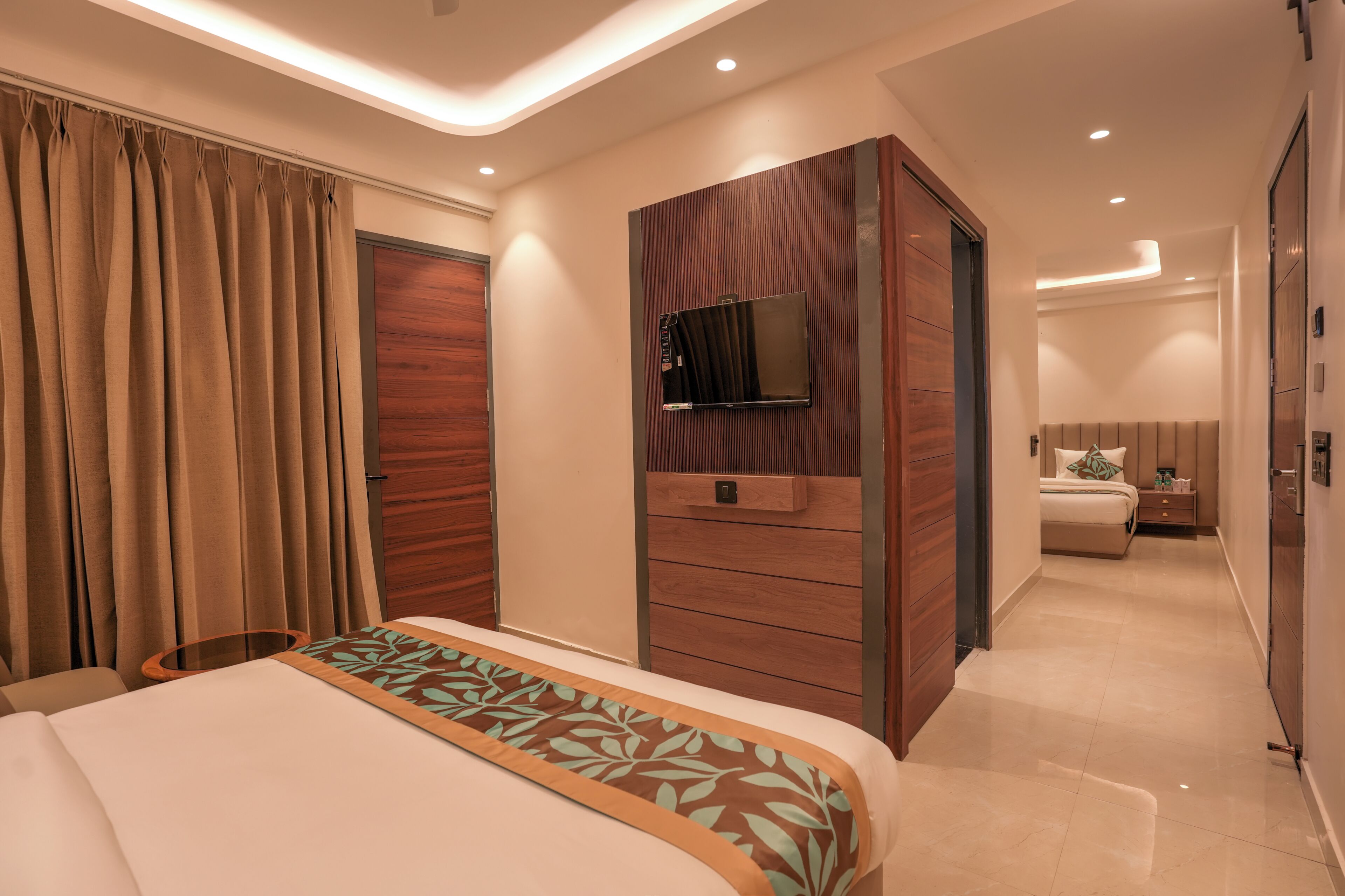 A modern hotel room with a bed, a TV, a wardrobe, and a bathroom in the background.
