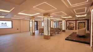 A spacious lobby with modern lighting, seating areas, and a large screen displaying a logo. - Madhuram Inn (Gautam Buddh Nagar)