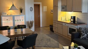 A modern apartment with a dining area, a living room with a sofa, a kitchen with appliances, and a hallway. - Directly south beach Fehmarn stylish apartment with terrace on the promenade (Fehmarn)