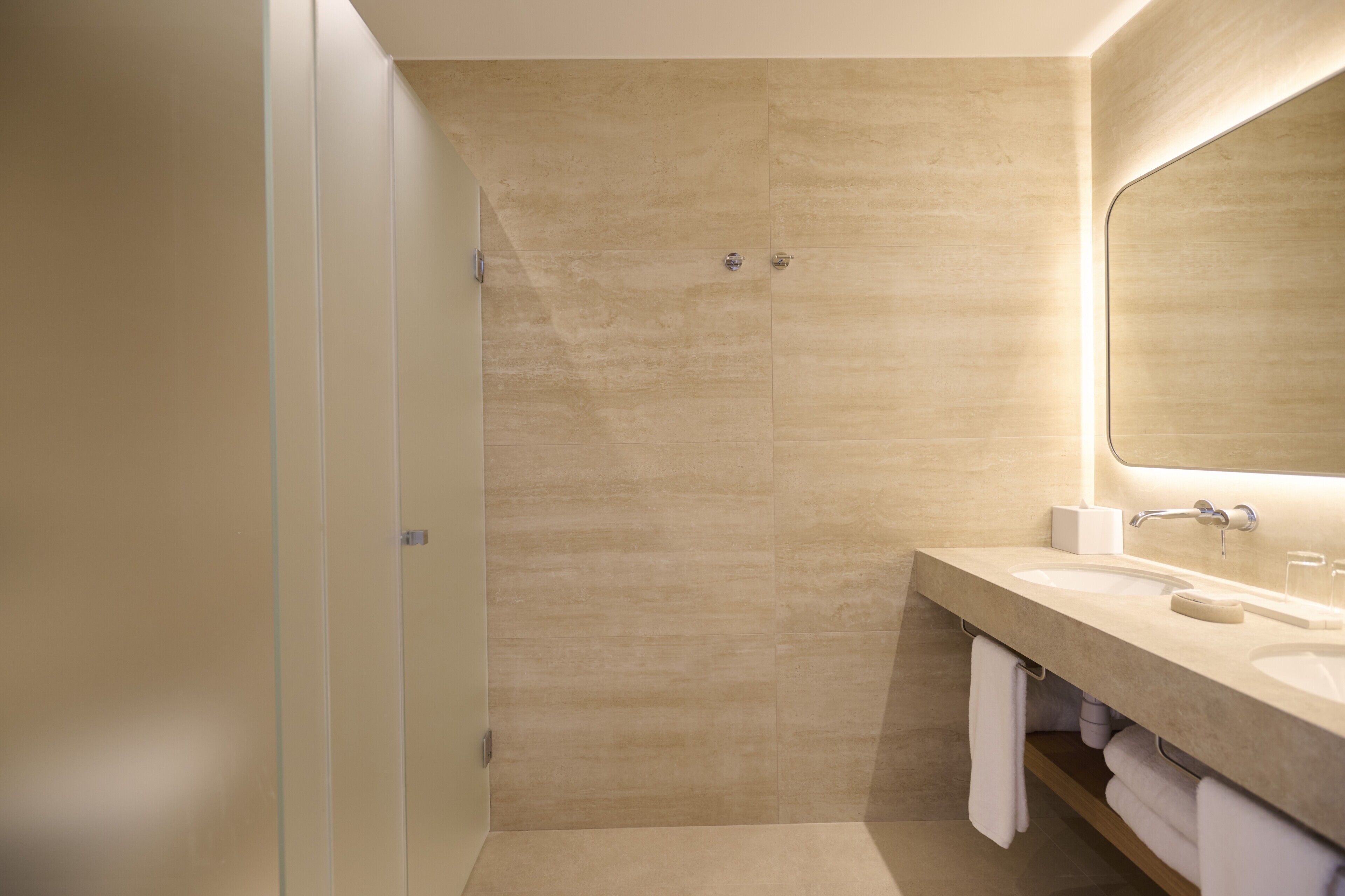 A modern bathroom with a large mirror, two sinks, and a shower area.