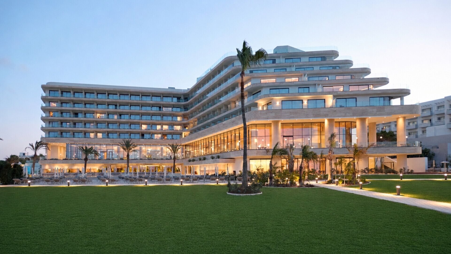 Un hotel moderno con varios pisos, un césped bien cuidado y una zona de piscina.