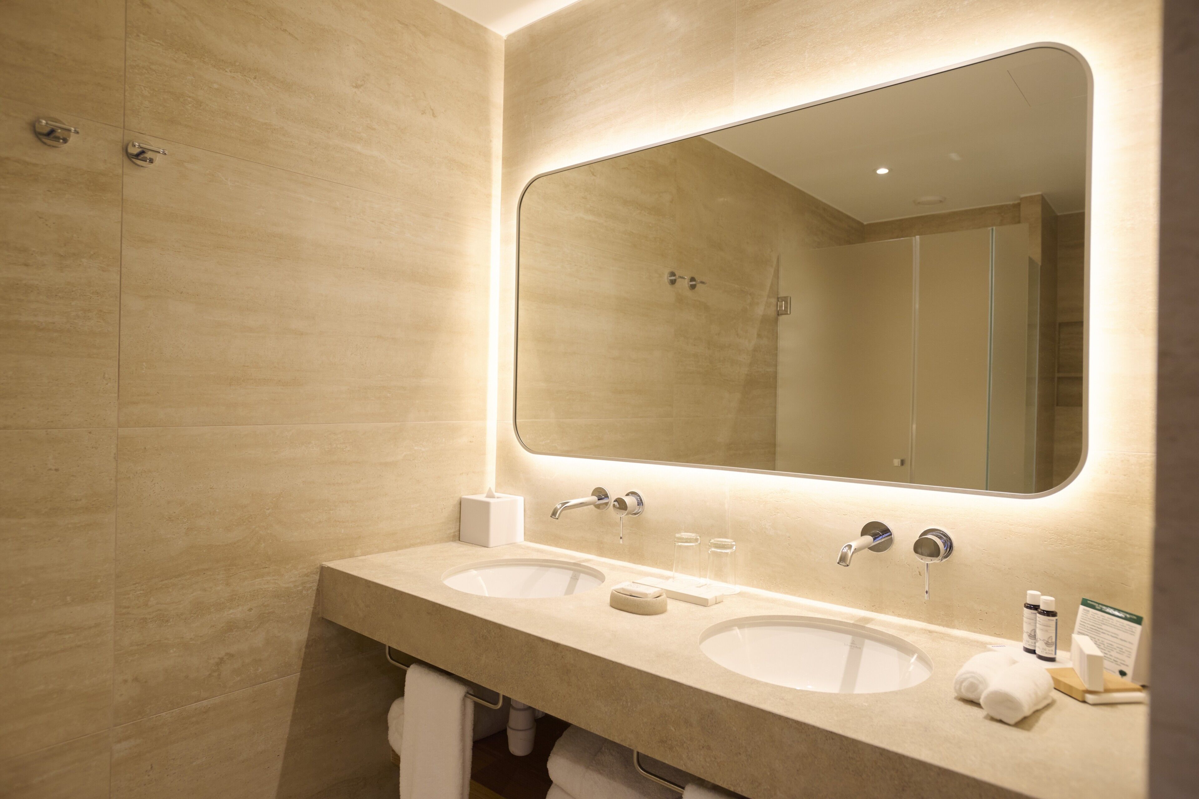 A modern bathroom with two sinks, a large mirror, and a towel rack.