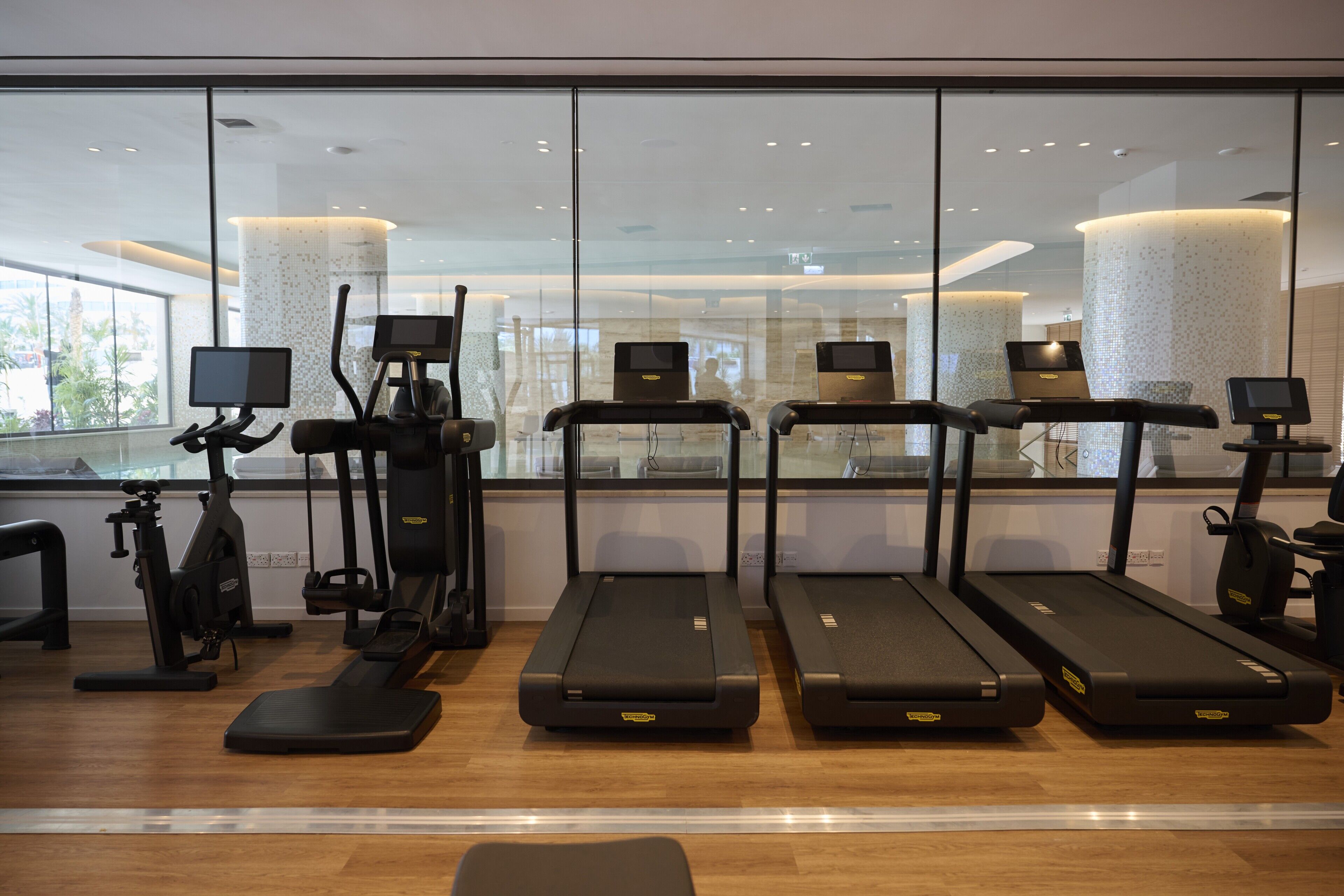 Un gimnasio con cintas de correr, elípticas y una máquina de remo.