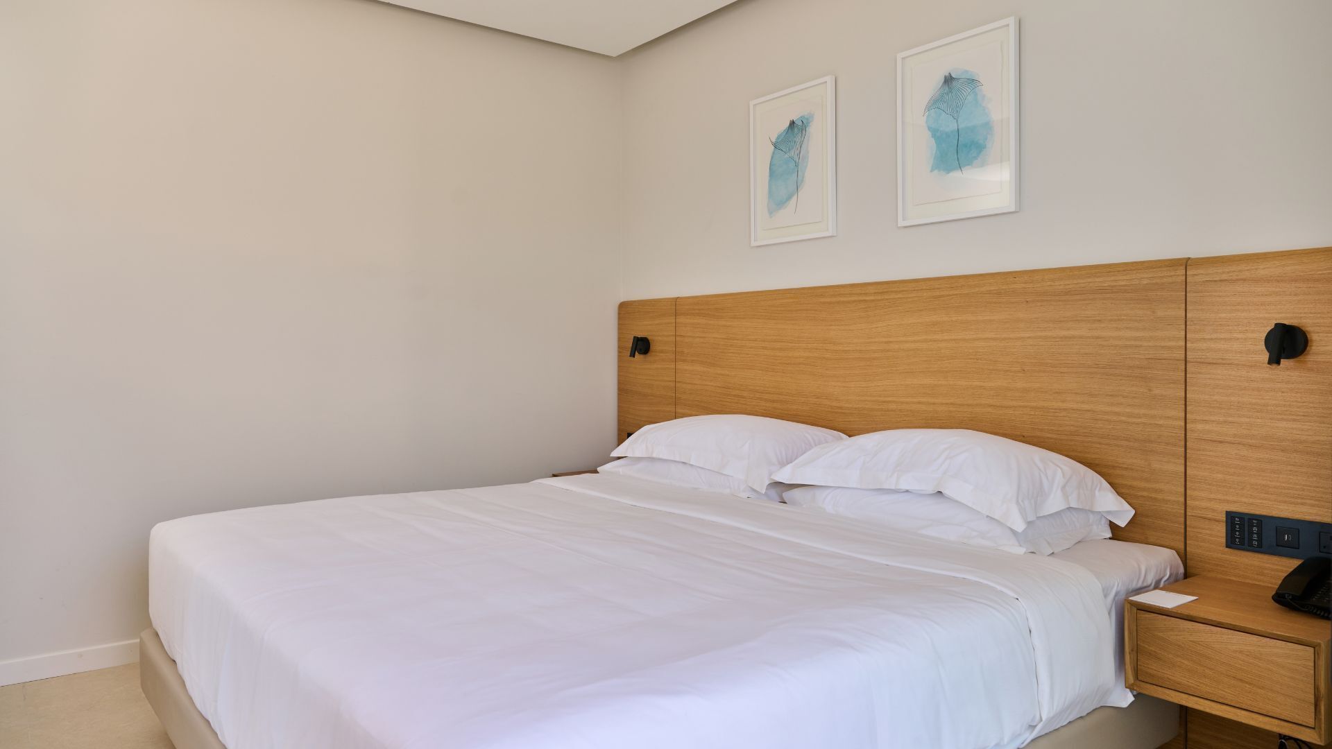 A neatly made bed with white linens, a wooden headboard, and a bedside table with a phone and a notepad.