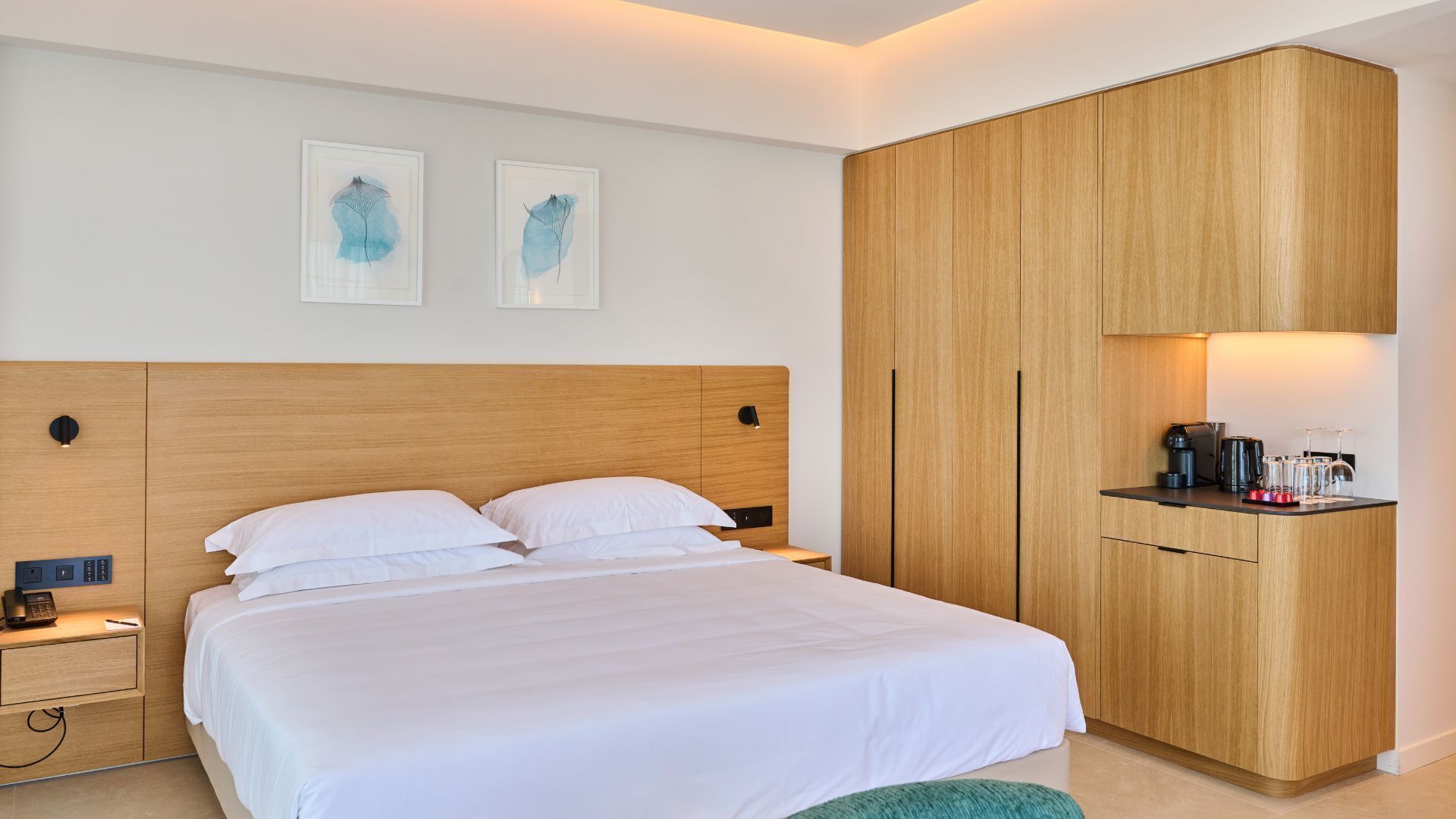A hotel room with a bed, bedside table, lamp, and a wooden wardrobe with a coffee maker on top.