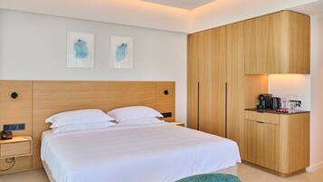 A hotel room with a bed, bedside table, lamp, and a wooden wardrobe with a coffee maker on top.