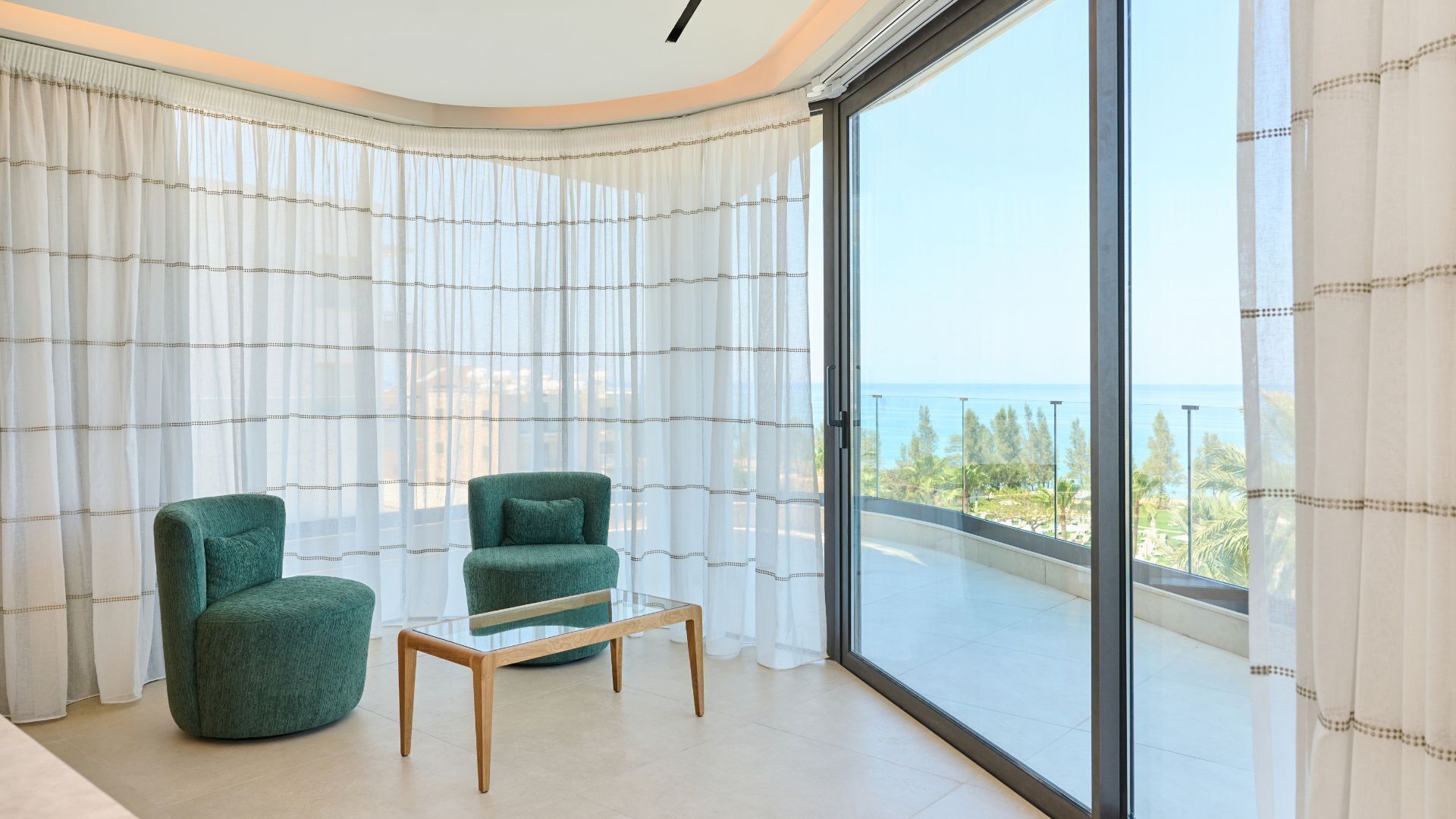 Un balcón con vista despejada al mar, dos sillones verdes y una mesa de centro de madera.