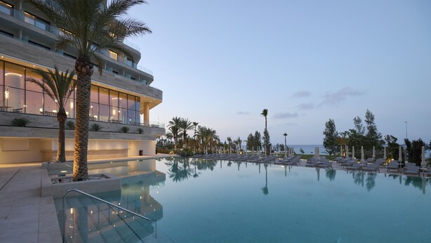 Ein modernes Hotel mit einem großen Infinity-Pool, Palmen und Meerblick.