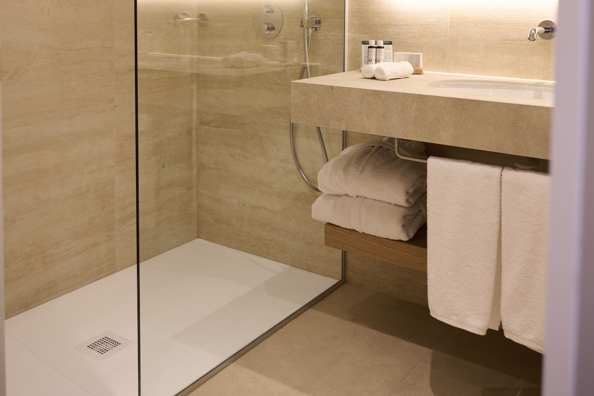 A modern bathroom with a glass-enclosed shower, a vanity with a mirror, and neatly folded towels.